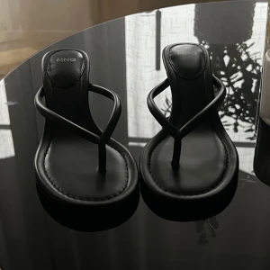 Svarta sandaler med klack från MNG - Svarta sandaler från MNG med tunna remmar och tårem. Skorna har en låg klack och rund tå. Normal i storleken. 