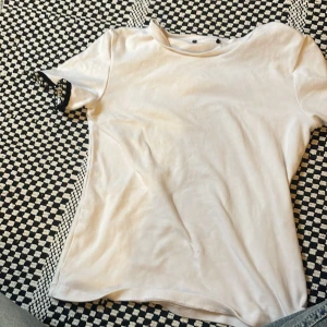 Vit t-shirt med pärldetaljer - Vit t-shirt i mjukt material med korta ärmar. Ärmsluten har svarta kanter dekorerade med pärlor som ger en unik och cool touch. Perfekt för dig som vill ha en basic tee med lite extra edge.