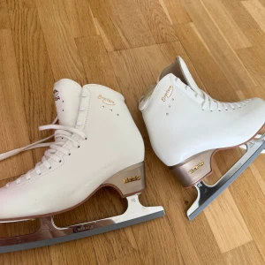 Vita konståkningsskridskor Edea - Snygga vita konståkningsskridskor från Edea med Mirage-blad från Jackson Ultima. Skorna har klassisk snörning, gulddetaljer och en beige häl. Tillverkade i syntetmaterial och perfekta för dig som vill glänsa på isen. Endast använda vid två tillfällen, i mycket fint skick. Inköpta för 4800 kr, säljes nu för 4500 kr. Två små repor på sidan av ena skridskon (se bild)  Kan eventuellt behöva slipas beroende på preferens Högkvalitativa och bekväma skridskor, perfekta för både nybörjare och mer erfarna