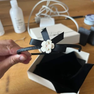 Dolce & Gabbana diadem - Snyggt svart diadem från Dolce & Gabbana med en dekorativ rosett och en vit blomma framtill. Diademet har en elegant och stilren look, perfekt för att lyfta din outfit. Kommer i originalask.