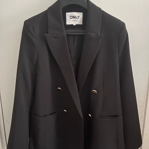 Svart kavajjacka från only Dam - Hej 👋 säljer nu min mammas snygga kavajjacka från only med fräscha guld knappar framtill. Jackan har två framfickor. Perfekt till allt möjligt men mest att att bara ge en liten touch till outfiten🥂Nypris 625kr! Har bara använt en gång bara, skriv vid minsta fundering och pris kan diskuteras