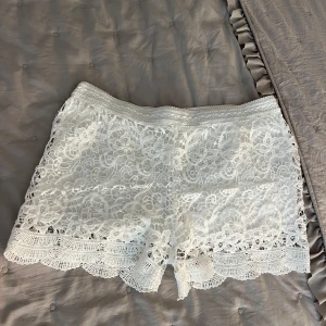 Vita snygga spetsshorts!!🥰 - Superfina vita shorts med blommig spets och vacker volangkant nertill. Perfekta för sommaren med sin romantiska och fräscha look. Elastisk midja för skön passform och snygg detalj med genombruten spets. Står storlek L/Xl men skulel säga att de är små i storleken så M skulle jag säga är rätt storlek.