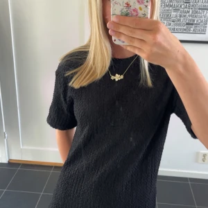 Svart kortärmad klänning - En svart, kortärmad klänning med strukturerat tyg och enkel, rak passform. Perfekt för dig som gillar stilrena och minimalistiska plagg. Klänningen har rund halsringning och är lätt att matcha med accessoarer.