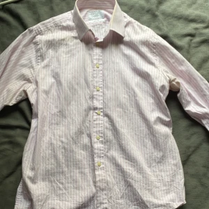 Randig skjorta Charles Tyrwhitt slim fit - Säljer en stilren slim fit skjorta från Charles Tyrwhitt med tunna rosa och vita ränder. Skjortan har klassisk krage, långa ärmar och knäppning framtill. Perfekt för dig som gillar en clean och dressad look.