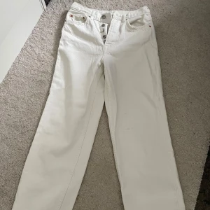 Vita raka jeans från Zara - Snygga vita jeans med raka ben och klassisk femficksdesign från Zara. Byxorna har knäppning med flera silverfärgade knappar och en ljus läderpatch bak i midjan. Perfekta för en clean och fräsch look året runt. De är insydda i midjan, endast litegrann.