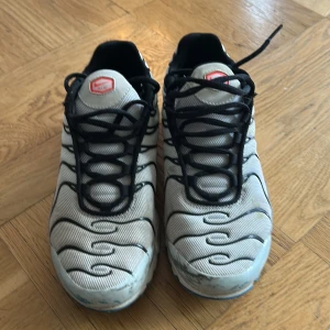Nike Air Max Plus Tn vit/svart/röd - Nike Air Max Plus Tn sneakers i vitt mesh med svarta vågformade detaljer och röda accenter. Skorna har svart snörning, synlig Air Max-sula och Tn-logga bak. Snygg och sportig modell som sticker ut med sin unika design och coola färgkombination.