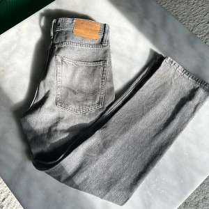Grå loose fit jeans Jack & Jones - Snygga grå jeans från Jack & Jones i loose fit-modell. Jeansen är i bomull och har en läderpatch bak i midjan. Perfekta för dig som gillar avslappnad stil och vill ha ett par bekväma jeans. Inte använda många gånger, bra skick på dom 27/30 i storlek. Hör av er vid frågor😊