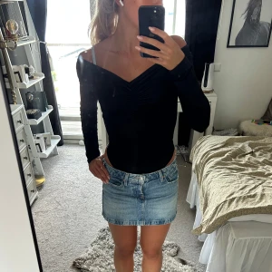 Svart body från BikBok XS - Säljer en svart body från BikBok i storlek XS. Toppen har lång ärm, v-ringning och snygg rynkdetalj framtill. Sitter tight och har offshoulder-design som ger en trendig look. Perfekt att styla med jeans eller kjol.