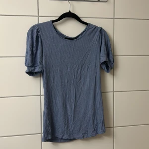 Blå ribbad topp med puffärm - Snygg blå topp med puffiga korta ärmar och rund halsringning. Tyget är ribbat och ger en cool struktur. Perfekt för dig som gillar en enkel men trendig stil.