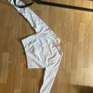 Vit långärmad topp i polyamid - Säljer en vit långärmad topp i stretchigt material med ribbade muddar. Tillverkad i 90% polyamid och 10% elastan, vilket gör den mjuk och följsam. Perfekt för lager-på-lager eller som basplagg. Enkel och clean design som passar till det mesta.