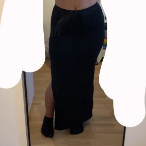 Svart långkjol med slits SHEIN - Svart långkjol från SHEIN i stretchigt material. Kjolen har hög midja, tight passform och en snygg slits på sidan som ger en trendig look. Perfekt för dig som gillar stilrena plagg med lite edge. Använd 1 gång. Storlek S passar M. 