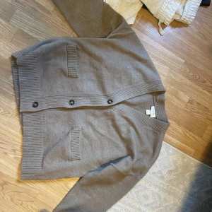 Beige kofta från Monki XS - Snygg beige kofta från Monki i storlek XS. Koftan har ribbade muddar, två fickor framtill och stängs med knappar. Perfekt för lager-på-lager och chill vibes. Materialet känns mjukt och är troligtvis bomull eller syntet.