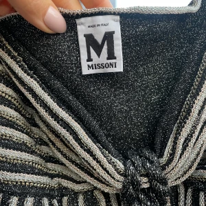 Missoni-klänning - Supersnygg mini-klänning från Missoni med glittriga svarta och silverfärgade ränder. Klänningen är en bandeu men det går att knyta snörerna run halsen också.  Nypris ligger runt 6000kr