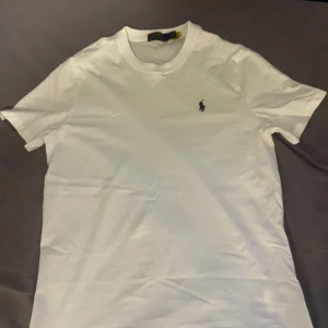Vit t-shirt från Polo Ralph Lauren - Klassisk vit t-shirt från Polo Ralph Lauren med broderad logga på bröstet. T-shirten har rund halsringning och korta ärmar. Tillverkad i mjuk bomull som känns skön mot huden. Perfekt basic-plagg med stilren design. Storlek L men skulle säga att den sitter som M :). Aldrig använd
