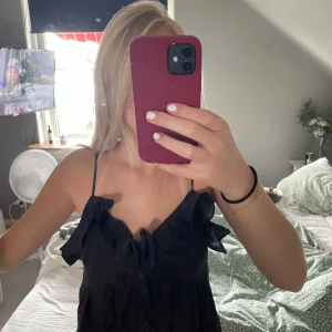 Svart klänning med volang - Supersöt svart klänning med tunna axelband och volangdetaljer vid bysten. Klänningen har en lätt rynkad look och en luftig passform som känns både chill och trendig. Perfekt för dig som gillar en enkel men ändå snygg stil. 💞