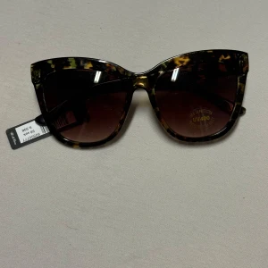 Bruna leopardmönstrade solglasögon - Snygga solglasögon från Wet Glam med brunmelerad båge i klassisk cat eye-form. Leopardmönstret ger en trendig vibe och glasen har UV400-skydd. Perfekta för att lyfta din stil på soliga dagar.