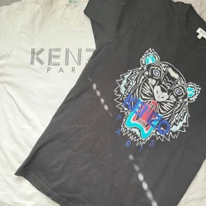 Kenzo t-shirts XS - Två snygga Kenzo t-shirts i bomull, en svart med ikoniskt tigertryck i blått, turkost och rött samt en vit med stilren Kenzo Paris-logga. Båda har en slim passform och kort ärm. Äkta och ny pris runt 1000kr per T-shirt. Skick är bra lite sliten men inget som märks. Köp en av dem för 459kr eller båda för 759kr.