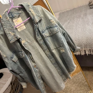 Oversized ljusblå jeansjacka Amisu - Säljer en oversized ljusblå jeansjacka från Amisu med slitna detaljer och råa kanter. Jackan har stora bröstfickor, knappar framtill och lång ärm. Perfekt för dig som gillar en chill och trendig look.