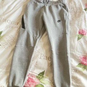 Gråa Nike tech fleece byxor - Snygga gråa Nike tech byxor i strl S. Detta är den gamla modellen som är lite mer slim fit än de nya modellerna. Rekommenderar dessa om du har xs i de nya modellerna. Ganska sällsynt att få tag på. Byxorna är i bra skick.