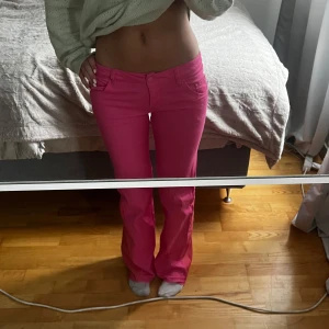 Lågmidjade rosa bootcut jeans - Säljer ett par riktigt snygga rosa jeans med bootcut-modell och låg midja. Byxorna har klassisk femficksdesign och stängs med knapp och dragkedja. Perfekta för dig som vill sticka ut med färg och ha en trendig siluett.