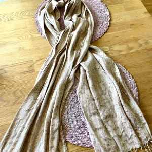 Champagnefärgad glittrig halsduk - Snygg och mjuk halsduk i champagnefärgat tyg med glittriga detaljer. Lång och lätt att styla på olika sätt, perfekt för att lyfta din outfit med lite extra shine. Materialet känns lent och följsamt mot huden.