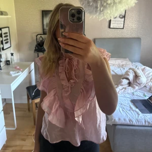 Ljusrosa volangblus med knyt - Supersöt ljusrosa blus med volanger längs v-ringningen och knytband vid halsen. Luftig och lätt i materialet, perfekt för vår och sommar. Blusen är köpt från Kappahl. Har aldrig använt den utan bara testad och lappen är kvar.. Den är i storlek S, men säljer även en i XS också. Nypris 399kr🤍