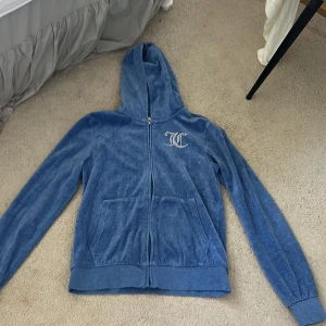 Blå hoodie Juicy Couture - Blå hoodie från Juicy Couture med glittrande logga på bröstet och stor Juicy Couture-text i strass på ryggen. Den är super skön och aldrig använd.