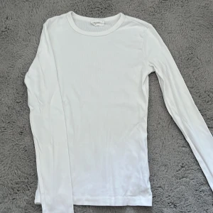 Vit ribbad långärmad tröja Gina Tricot - En basic vit långärmad tröja från Gina Tricot, basically basics-kollektionen. Tröjan är ribbad och har en rund halsringning. Perfekt att styla med jeans eller kjol för en clean och enkel look.