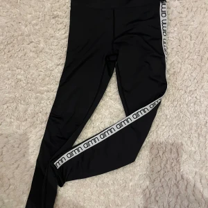 Svarta Aim'n leggings med logga - Svarta leggings från Aim'n med vit logga längs sidorna. Tight passform och hög midja. Snygga och stilrena. 