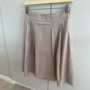 Beige kjol från Esprit - Snygg beige kjol från Esprit med diskreta veck framtill. Kjolen har en klassisk midja. Aldrig använd.