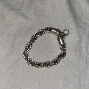 Tjockt tvinnat silverfärgat armband - Säljer ett snyggt armband cordel i silverfärg med tvinnad kedja och robust lås. Armbandet har en chunky känsla och passar perfekt för dig som gillar stilrena accessoarer med lite edge. Perfekt att bära ensam eller att matcha med andra smycken.