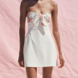 Vit och blommig kort bandeauklänning  - Superfin axelbandslös/ bandeau kort klänning i vitt med blommigt mönster och knyt framtill som är slutsåld i storlek S på Zaras hemsida. Sitter så snyggt perfekt nu i sommar!!