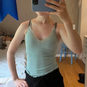 Ljusgrön ribbad linnetopp från Amisu - Supersöt ljusgrön ribbad linnetopp från Amisu med spetsdetaljer längs v-ringningen. Tunt och stretchigt material med smala axelband, perfekt för varma dagar. Snygg croppad passform som ger en fräsch och trendig look.