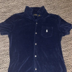 Mörkblå frottéskjorta från Polo Ralph Lauren - Mjuk och skön mörkblå skjorta i frotté från Polo Ralph Lauren perfekt nu till sommaren. Skick 9/10 Har du fler frågor är det bara att höra av dig!