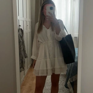 By Malina klänning - Superfin vit kortklänning med volangkant och knyt i midjan. Klänningen har långa ärmar. Perfekt för sommarens alla tillfällen. Väldigt skön och passformen går att justera med bandet i midjan. Jag är 156 cm lång för referens o har vanligtvis storlek xs. Klänningen är endast använd en gång, på min student, men köpte den här på plick av en tjej som även hon bara hade använt den en gång. Går att både klä upp och ner klänningen! Inga defekter 
