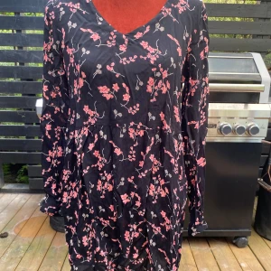 Blommig svart klänning från Kaffe 34 - Söt tunika med långa ärmar och ett blommigt mönster i rosa och grått på en svart bakgrund. Tunikan har en v-ringning och en ledig passform.  L: 89cm ﻿Bystvidd: 50cm  Inga bilder när den sitter på mig! Katter finns i hemmet!