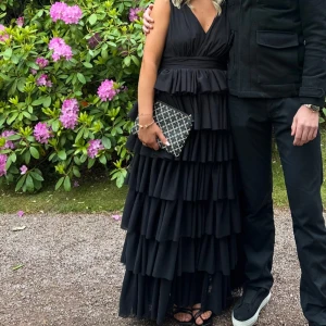 Svart långklänning med volanger - Supersnygg svart långklänning med djup v-ringning och flera lager volanger som ger en riktigt festlig känsla. Klänningen är i storlek 40 men skulle mer säga att den är som en 38! 