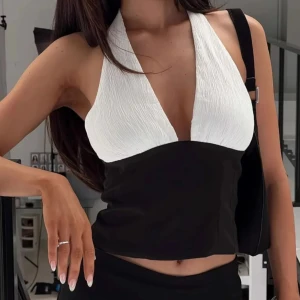 Svart och vit halterneck topp - Snygg tvåfärgad halterneck topp med djup v-ringning. Toppen är svart nedtill och har en vit, lätt skrynklig överdel. Croppad modell som ger en modern och trendig look, perfekt för att sticka ut.