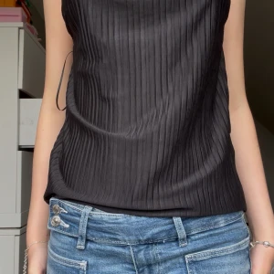 Svart plisserad linnetopp Gina Tricot - Säljer en svart plisserad linnetopp från Gina Tricot i storlek XS. Toppen har tunna axelband som korsas i ryggen och en öppen rygg för en snygg look. Materialet är lätt och glansigt, perfekt för att sticka ut lite extra. Aldrig använd!