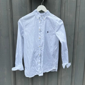 Vit skjorta från Ralph Lauren - Klassisk vit skjorta från Ralph Lauren med button down-krage och broderad logga på bröstet. Strl: 18 i barn, sitter som xs. Fråga vid funderingar. Pris kan diskuteras.