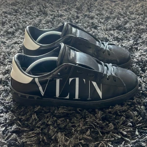 Valentino skor - Snygga svarta sneakers från Valentino Garavani med stor vit VLTN-logga på sidan och vit häl. Skorna har snörning, platt sula och är tillverkade i skinn. Perfekta för dig som gillar exklusiva och trendiga detaljer.