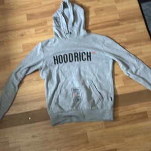Grå HOODRICH hoodie med tryck S - Snygg grå hoodie från HOODRICH med svart och rött tryck både fram och bak. Tröjan har huva, långa ärmar och praktisk ficka med dragkedja. Perfekt streetstyle med coola detaljer och skön passform. Priset är inte hugget i sten.