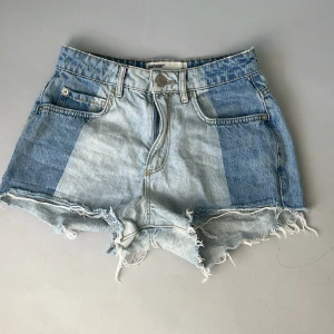 Patchade jeansshorts från Garage - Snygga ljusblå jeansshorts från Garage med patchad denimlook i olika blå nyanser. Shortsen har fransig, rå kant nertill och klassiska fem fickor. Perfekta för sommaren och ger en cool, avslappnad vibe.