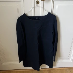 Mörkblå långärmad tröja från COS - En stilren mörkblå långärmad tröja från COS i rak modell med rund halsringning. Tröjan är enkel och minimalistisk, perfekt för dig som gillar clean look. Materialet känns mjukt och har en lätt struktur. Passar dig som gillar klassisk och tidlös stil.