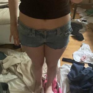 True Religion jeansshorts låg midja - Säljer ett par blå jeansshorts från True Religion med låg midja och råa kanter. Klassiska detaljer med stora bakfickor och synliga sömmar, samt knappstängning och bälteshällor. Perfekta för sommaren och riktigt snygga till en enkel topp. Pris går diskuteras!