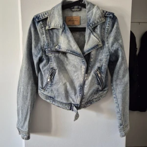 Acid wash jeansjacka från Denim - Snygg acid wash jeansjacka från Denim med cool bikerstil, dragkedjor och klassisk krage. Jackan har croppad passform och flera fickor med dragkedja. Perfekt för dig som vill sticka ut med en edgy look.