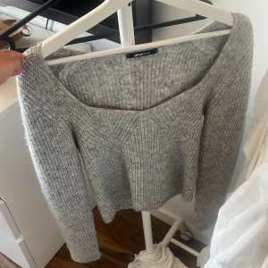 Grå stickad tröja Gina Tricot - Supermysig grå stickad tröja från Gina Tricot med bred, något fyrkantig ringning och ribbad struktur. Långärmad och perfekt för lager-på-lager under kyliga dagar. Snygg till både jeans och kjol för en chill look.