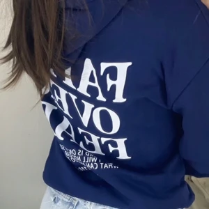 Marinblå hoodie Faith Over Fear - Marinblå hoodie med vit text 'Faith Over Fear' tryckt på både fram- och baksidan. Tröjan har huva med snörning och en stor magficka. Tillverkad i mjukt material, perfekt för kyliga dagar. Snygg och bekväm stil som passar till jeans eller leggings.