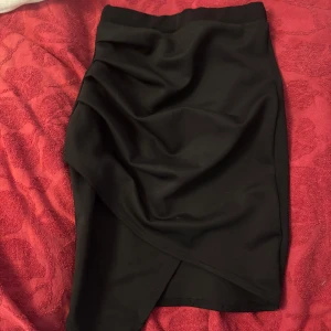 Svart omlottkjol med drapering - Snygg svart kortkjol med omlott-design och draperad effekt framtill. 