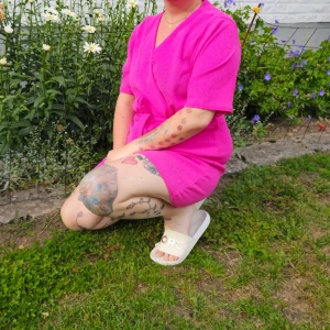 Rosa omlottjumpsuit Sisters Point XL - Superfin kort rosa omlott jumpsuit från Sisters Point i storlek XL. Jumpsuiten har knytband i midjan, v-ringning och korta ärmar. Materialet är lätt och stretchigt i 95% polyester och 5% elastan, perfekt för varma dagar.